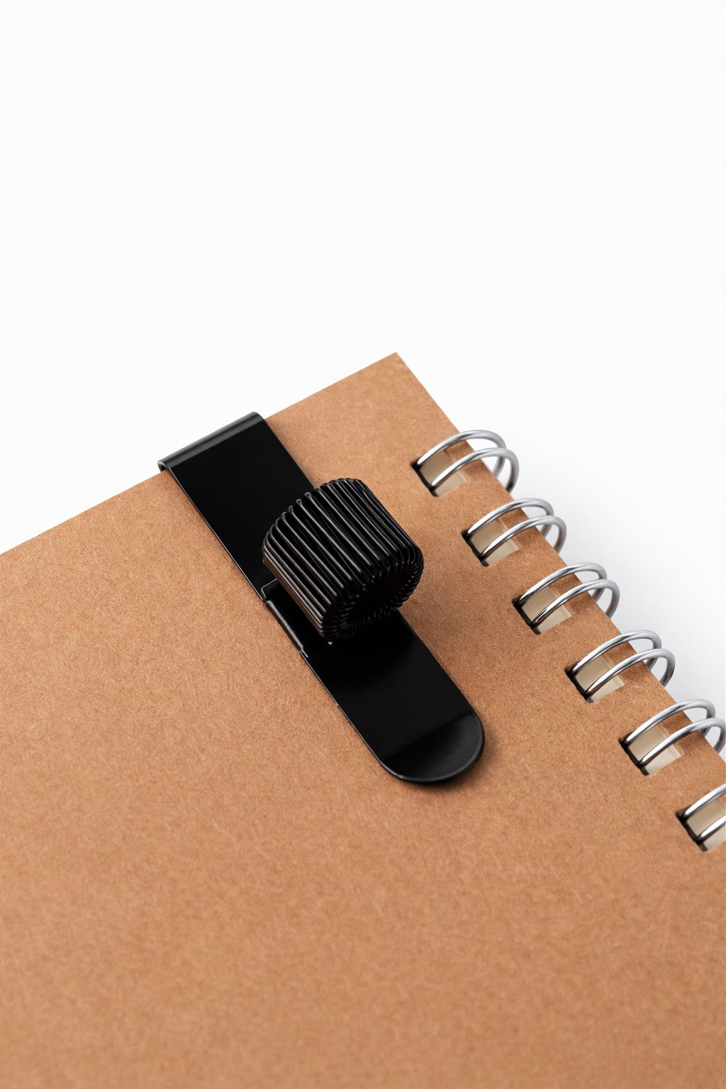Black pen holder clip on a brown notebook with a white background