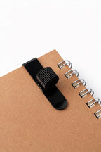 Black pen holder clip on a brown notebook with a white background